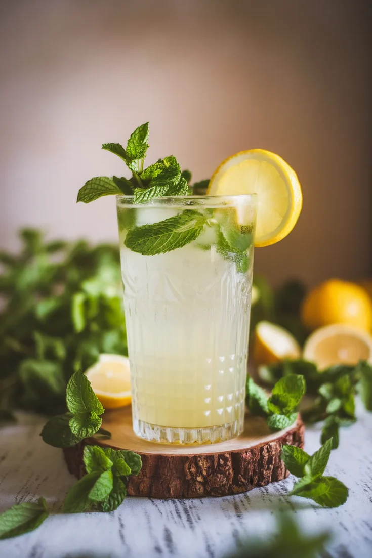 Refreshing lemonade with mint and lemon slice in a glass, perfect summer drink on a wooden coaster.