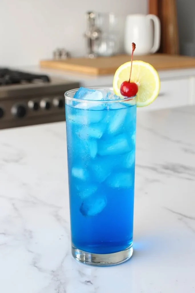 Refreshing blue cocktail with lemon and cherry garnish in a glass, perfect for summer on a marble countertop.