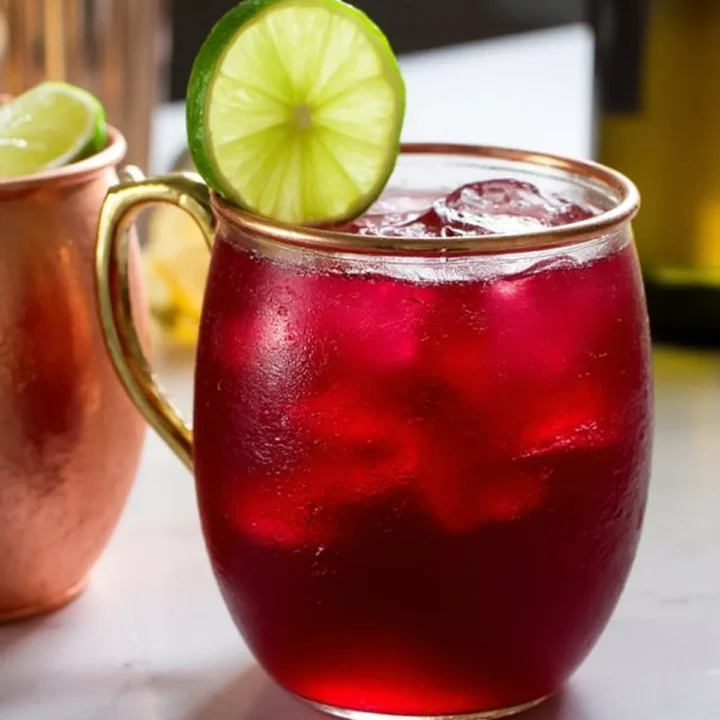 Red cocktail with lime garnish in a brass mug on a marble counter. Refreshing drink perfect for a hot day.