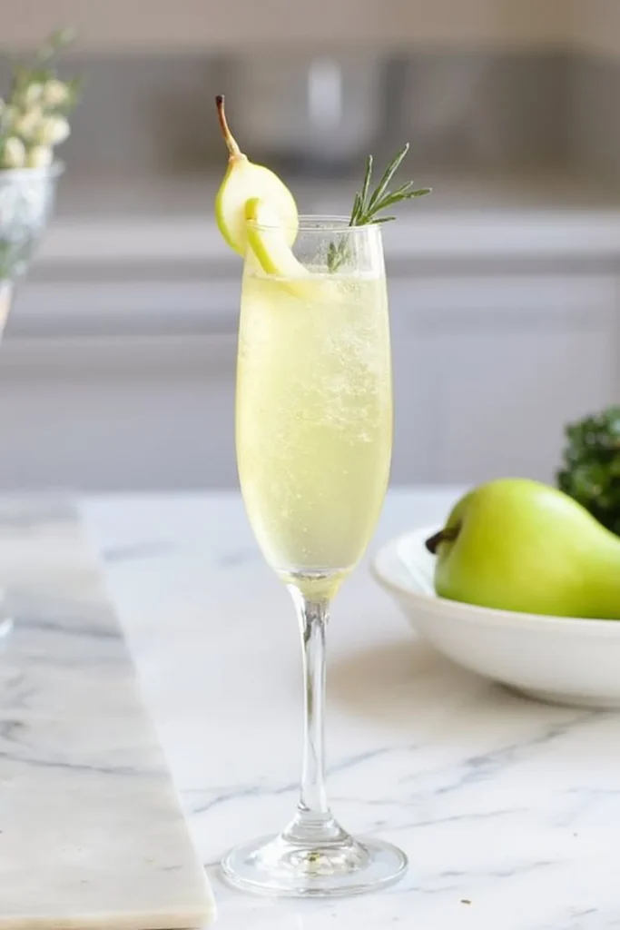 Champagne flute with pear cocktail and rosemary garnish on marble counter.