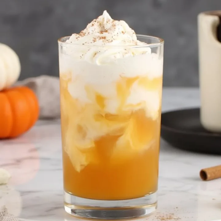 Creamy pumpkin spice drink topped with whipped cream on a marble surface, perfect for cozy autumn days.