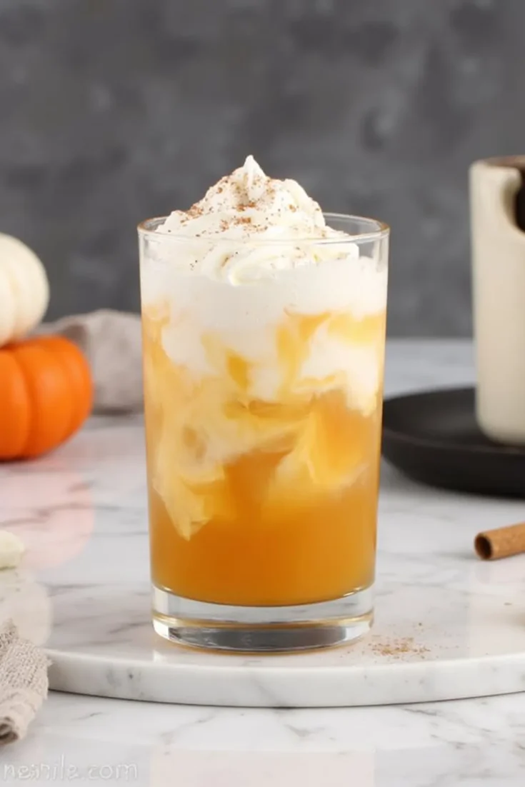 Creamy pumpkin spice drink topped with whipped cream on a marble surface, perfect for cozy autumn days.